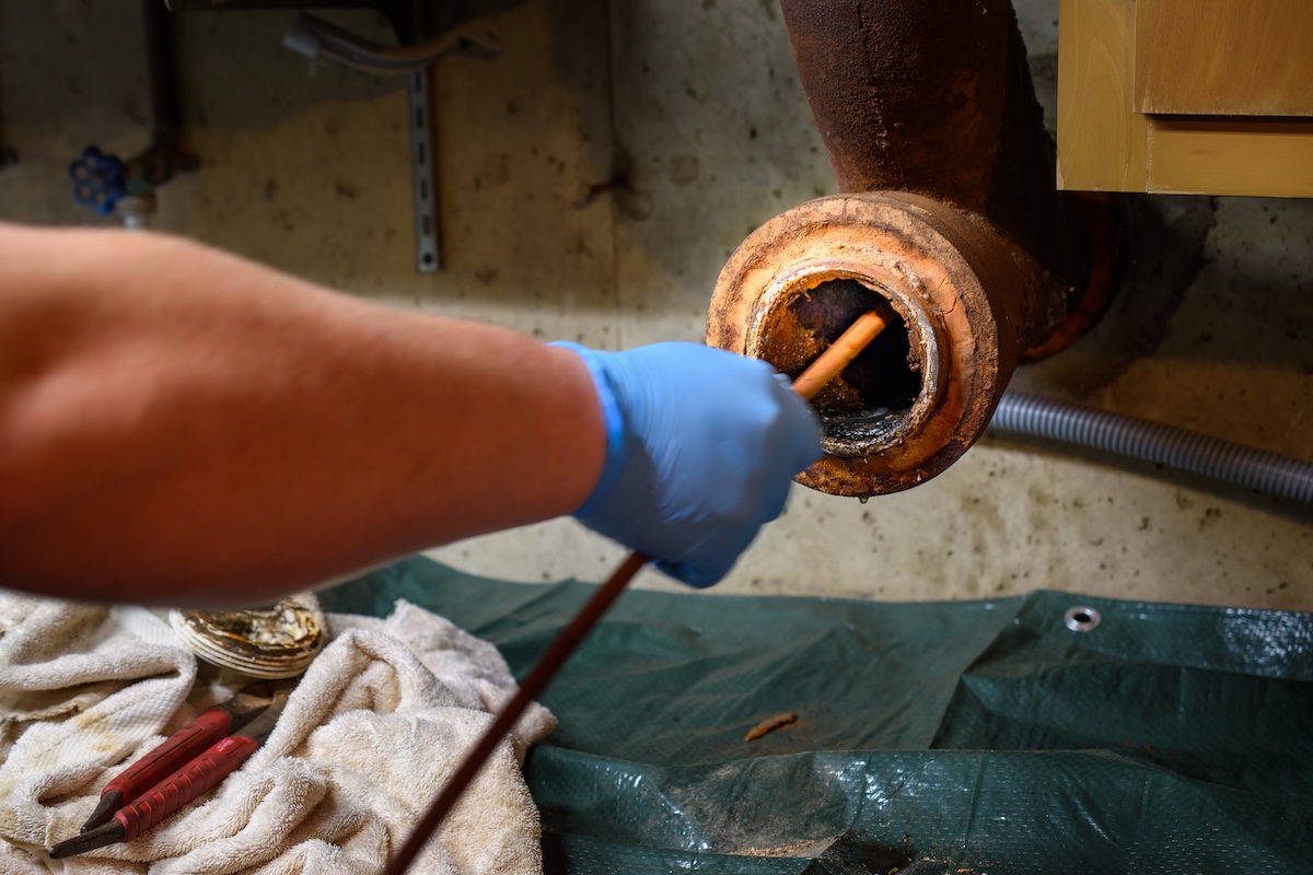 Hands of a plumber as he runs a camera scope and cleaning machine through the main pipe to unclog the drain to the Septic System. Hard-working tradesman.