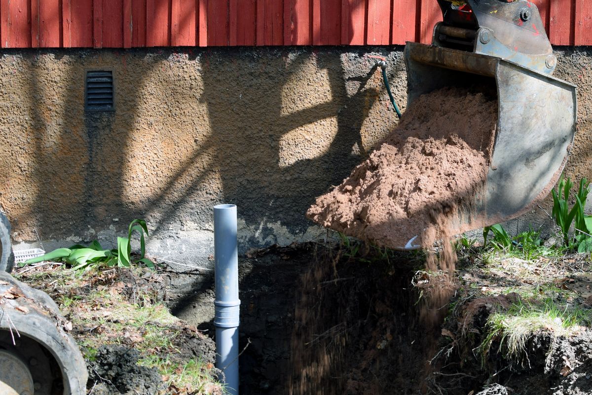 Excavator in construction site filling the sewer pipe trench with sand