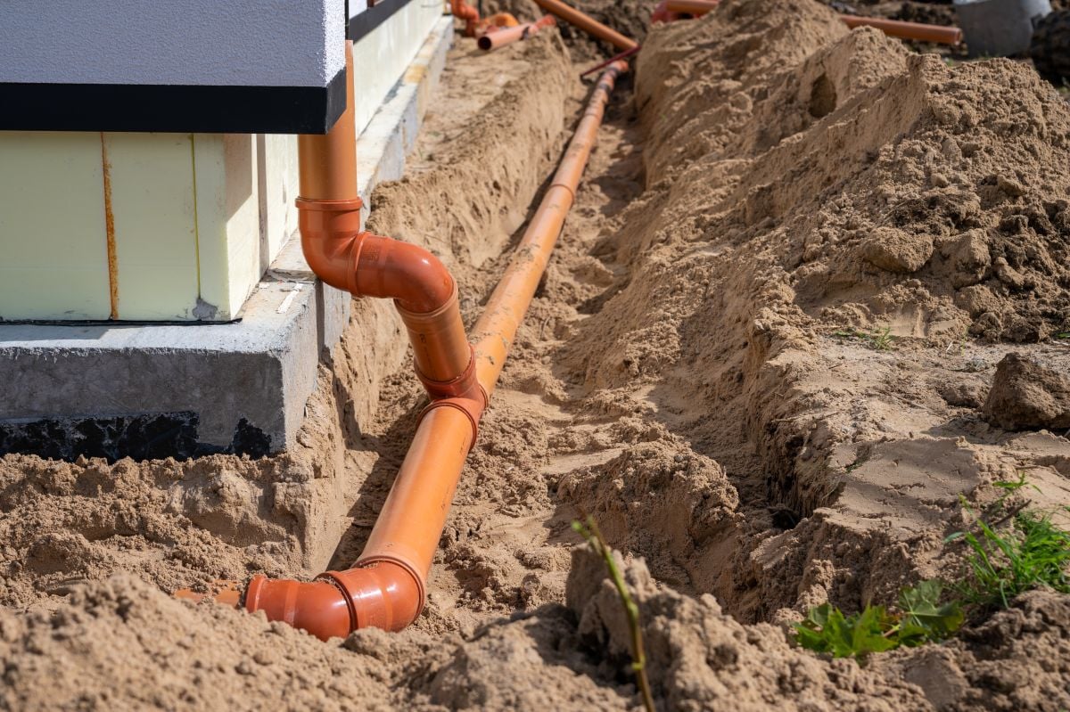 Underground drainage pipe installation next to residential building foundation during construction