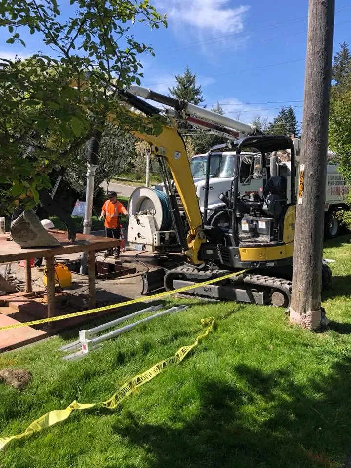 Excavator and crew working on underground utility repair near residential street with caution tape