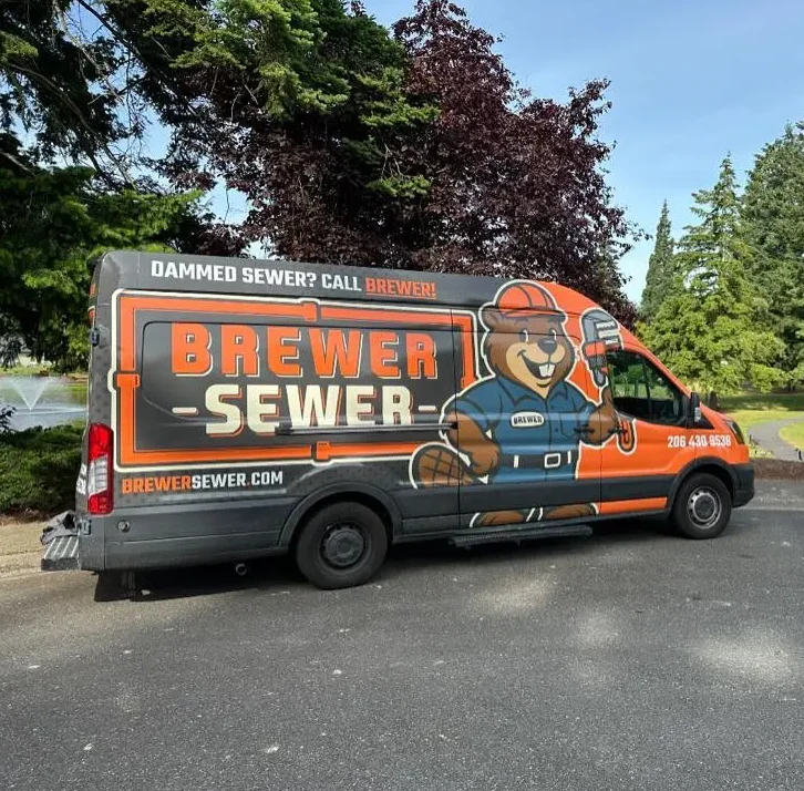 Brewer Sewer service van parked in park as worker sets up promotional sign near roadway