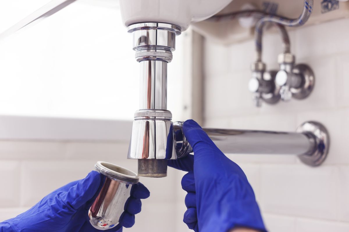 Plumber repairs and maintains chrome siphon under the washbasin