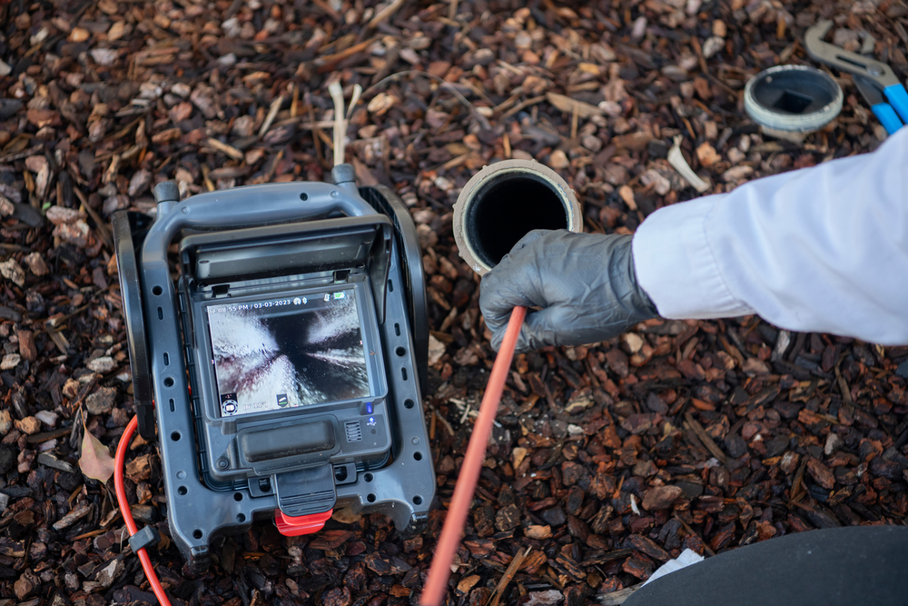 Technician performing sewer inspection with camera system inserted into outdoor drain cleanout pipe
