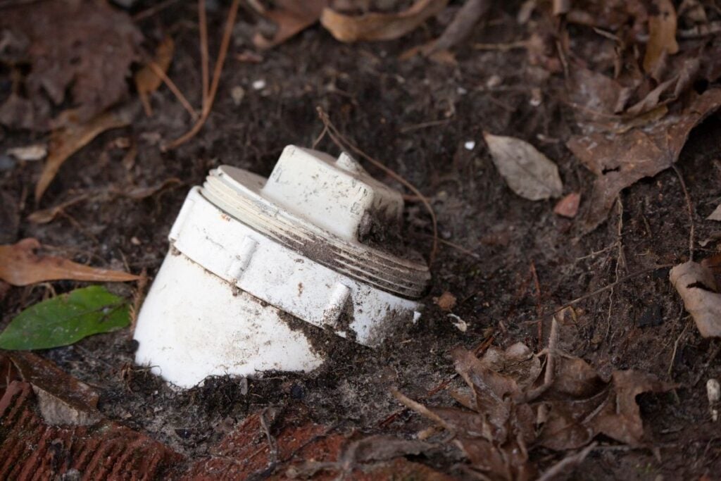 White PVC sewer cleanout pipe with screw cap in the ground outdoors