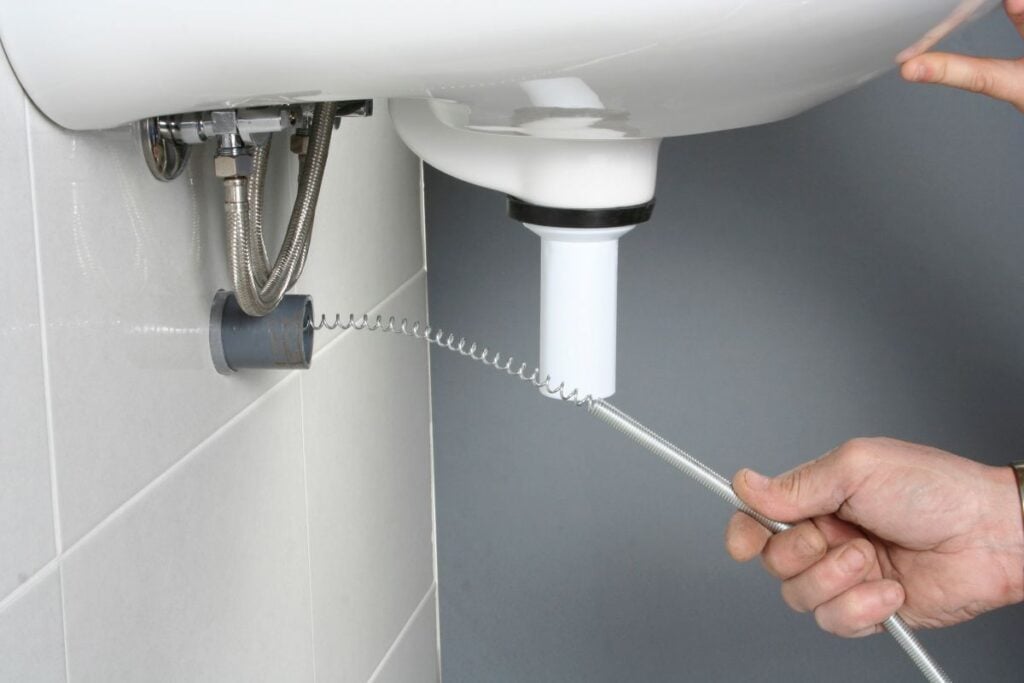 Plumber using a drain snake to unclog a sink