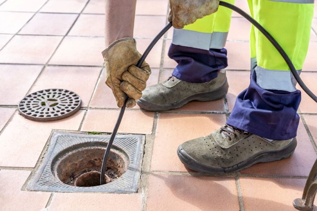 Sewer worker unclogging blocked yard drain with hydro jetting hose