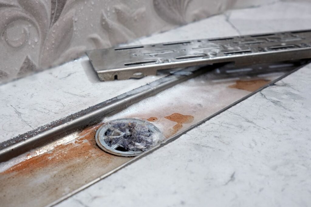 Clogged shower drain visible in open decorative metal