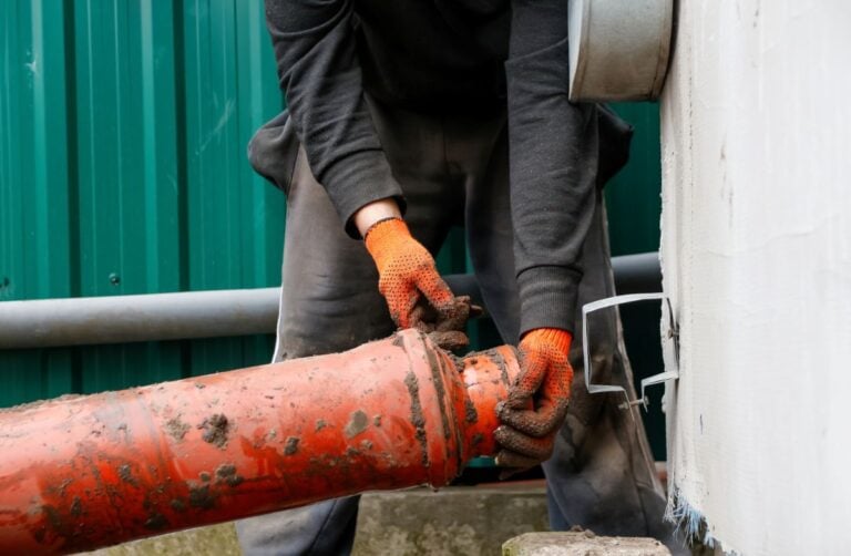 Plumber installing orange plastic sewage pipe outdoor.