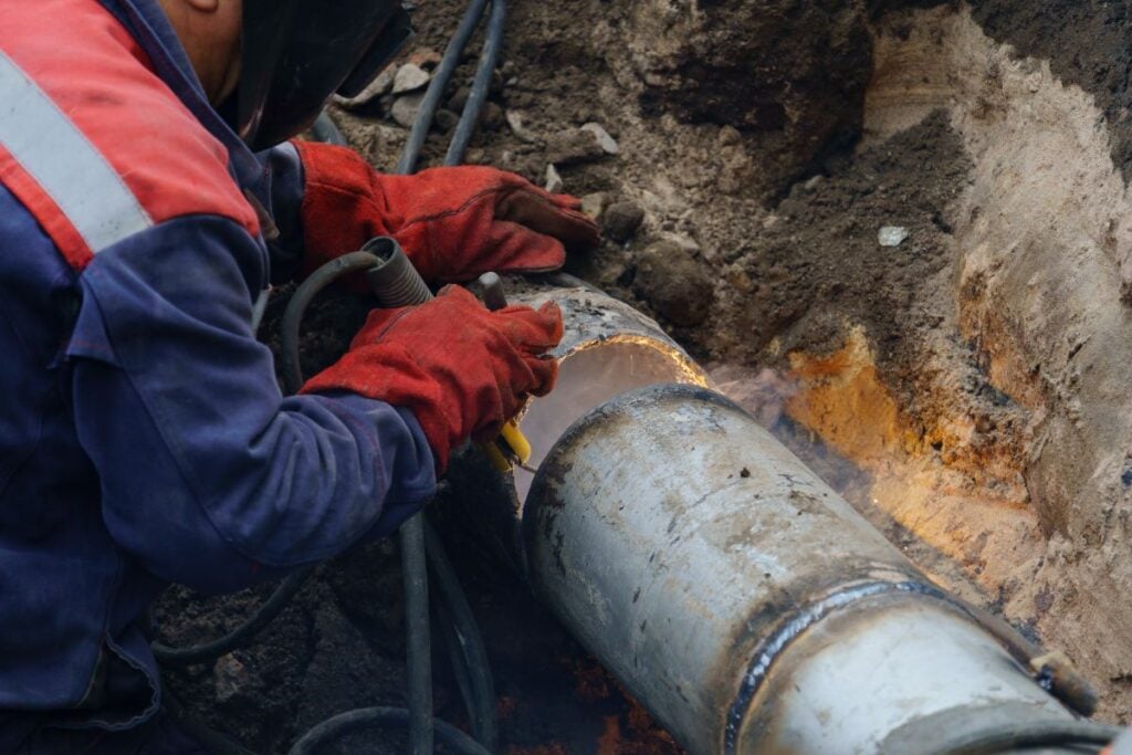 Plumber standing in pit is engaged in elimination of communal accident outdoors. Utility worker fixing broken water main.