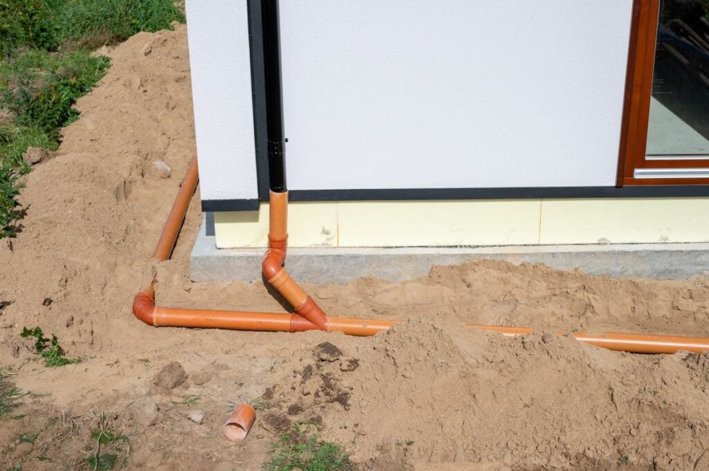 Underground drainage pipe installation next to residential building foundation during construction.
