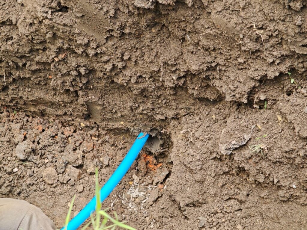 Close-up of blue plastic water pipe entering a drilled underground tunnel in a dirt wall. Horizontal directional drilling and trenchless utility installation process