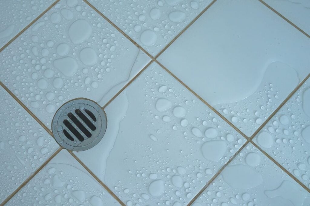 Top view of drainage hole stainless and shower water stain with wet floor on white tile background.