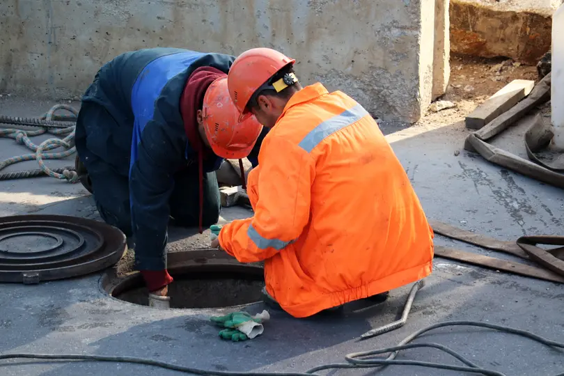 Workers over the open sewer hatch on a street. Concept of repair of sewage, underground utilities, water supply system